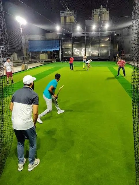 Friends playing cricket on a green turf under floodlights at night